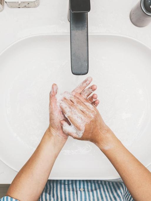 Blick von oben auf ein Waschbecken in dem sich eine Person die Hände wäscht.