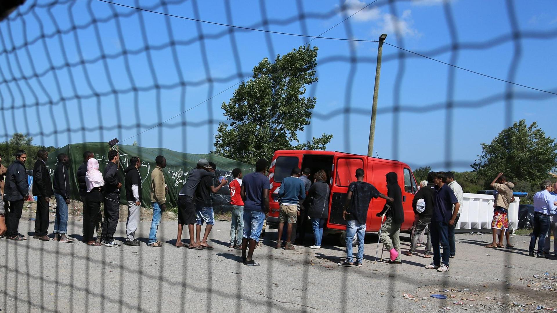 Hinter einem Zaun stehen in Calais Flüchtlinge