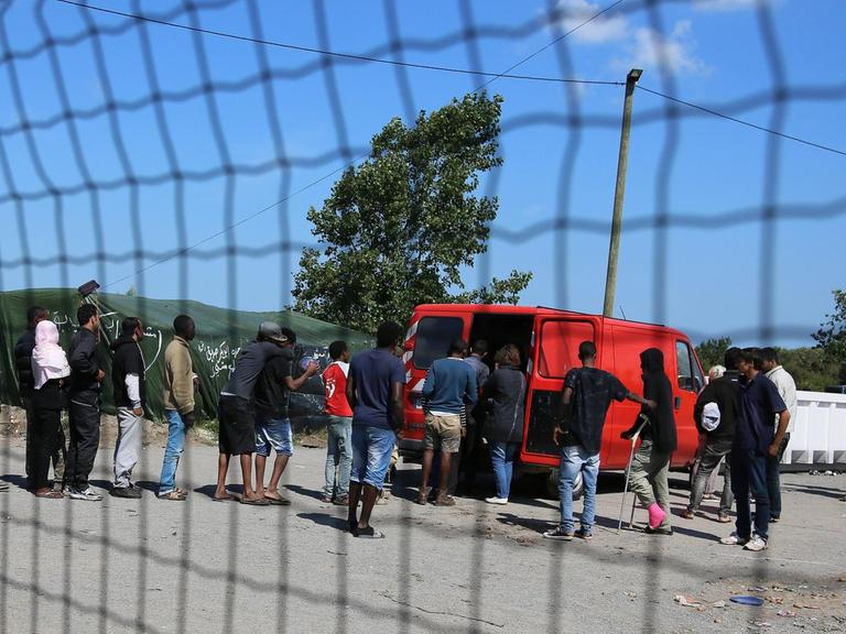 Hinter einem Zaun stehen in Calais Flüchtlinge