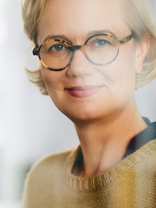 Die Geschäftsführerin der Uhrenfirma Nomos aus Glashütte in Sachsen, Judith Borowski, steht hinter eine Scheibe und lächelt in die Kamera.