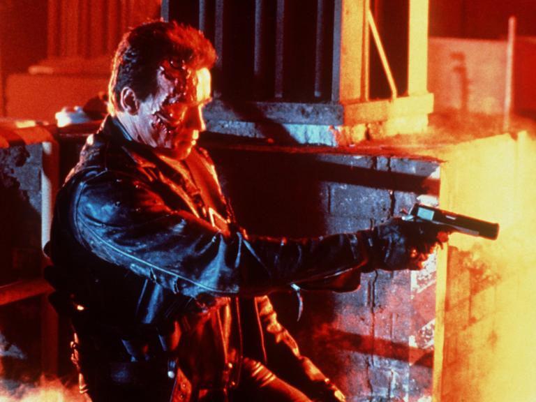 Arnold Schwarzenegger in einer Filmszene aus "Terminator ", umgeben von Feuer, schießend