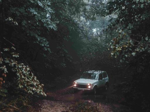 Ein weißes Auto mit Scheinwerfern mitten auf einem Waldweg.