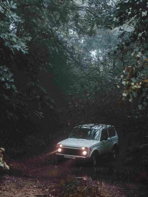 Ein weißes Auto mit Scheinwerfern mitten auf einem Waldweg.