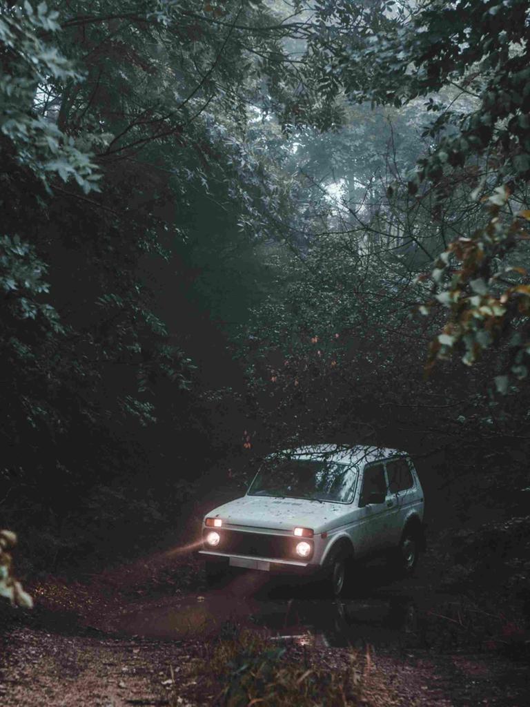 Ein weißes Auto mit Scheinwerfern mitten auf einem Waldweg.