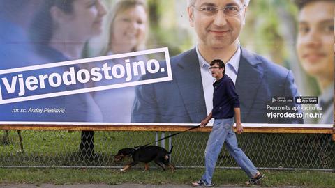 Ein Mann geht in der kroatischen Hauptstadt Zagreb mit seinem Hund an einem Wahlplakat der nationalkonservative Partei HDZ vorbei.