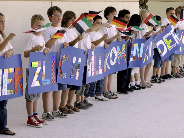 Schüler bei der Eröffnung der Deutschen Internationalen Schule in Abu Dhabi, Vereinigte Arabische Emirate. Sie halten Schilder, auf denen Herzlich Wilkommen zu lesen ist, in den Händen.