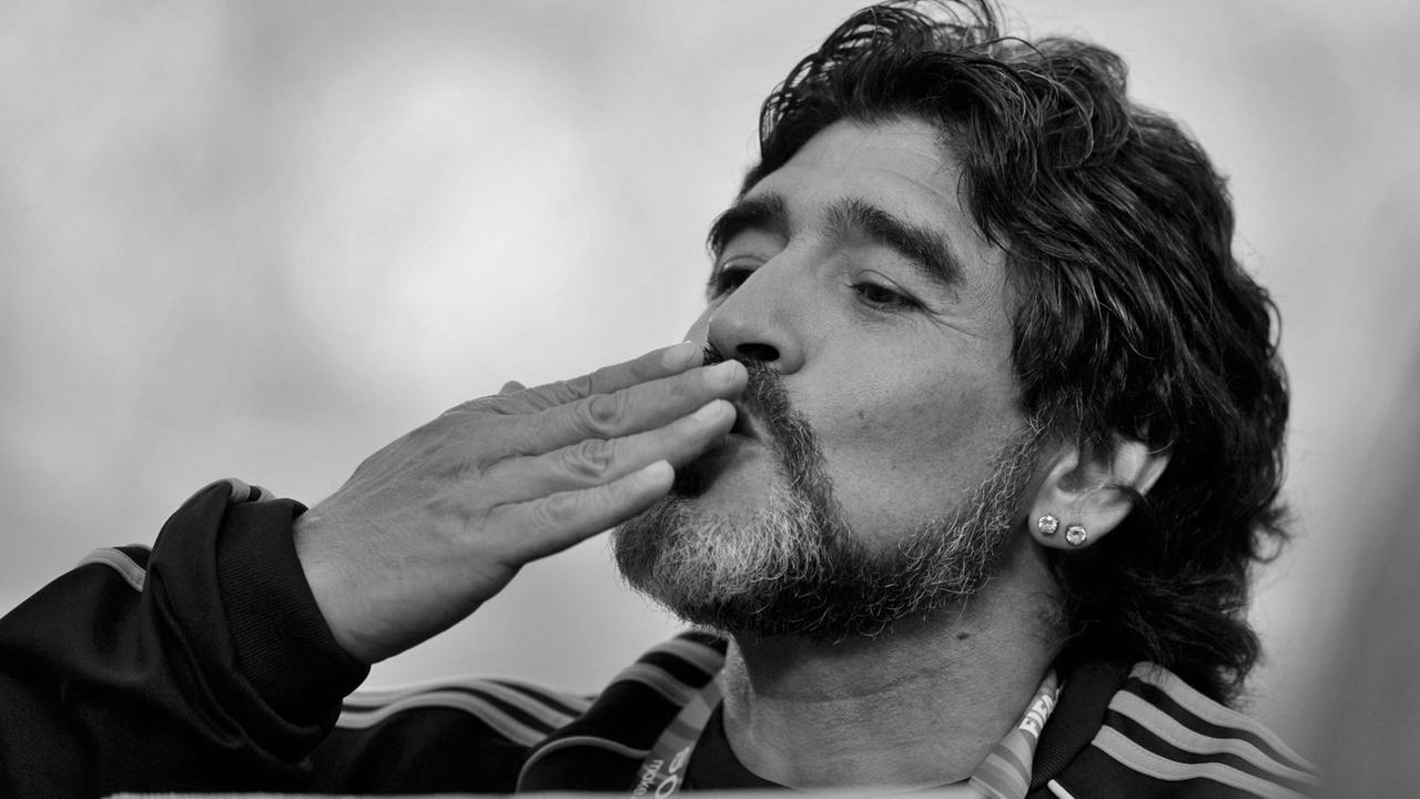 Schwarz-Weiß-Aufnahme von Diego Maradona. Er führt seine Hand zum Mund für einen Luftkuss. 