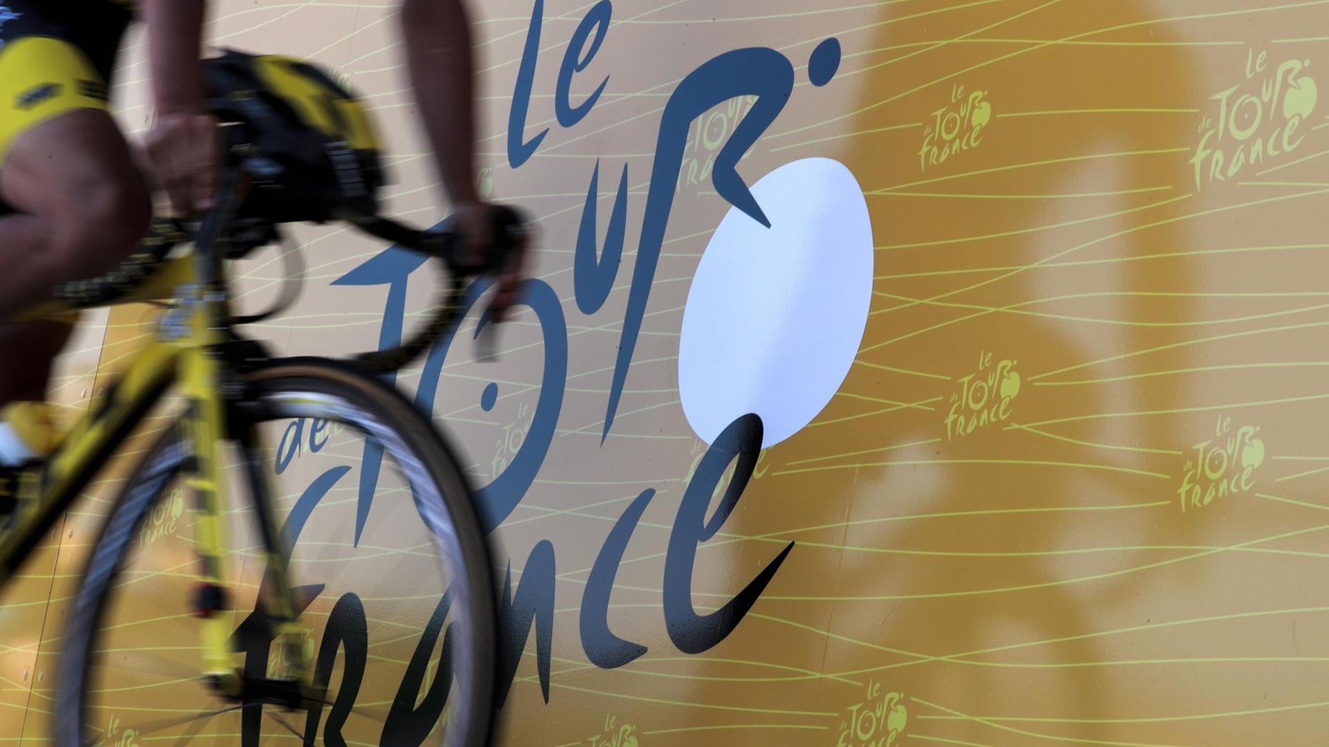 Ein Rennradfahrer vor dem Logo der Tour de France (8.7.)