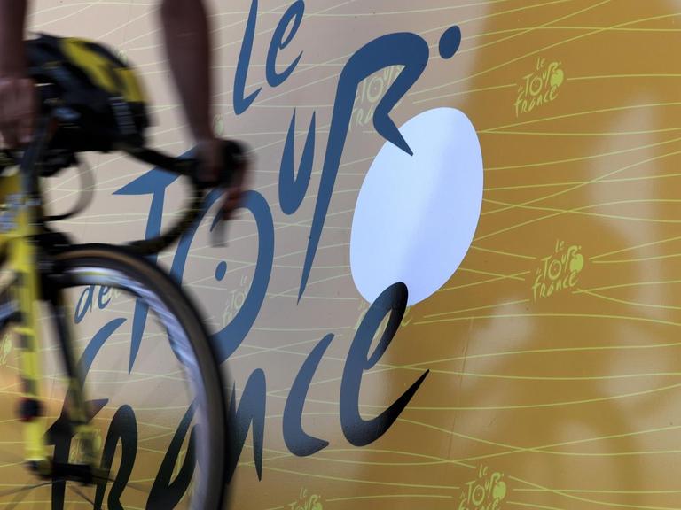 Ein Rennradfahrer vor dem Logo der Tour de France (8.7.)