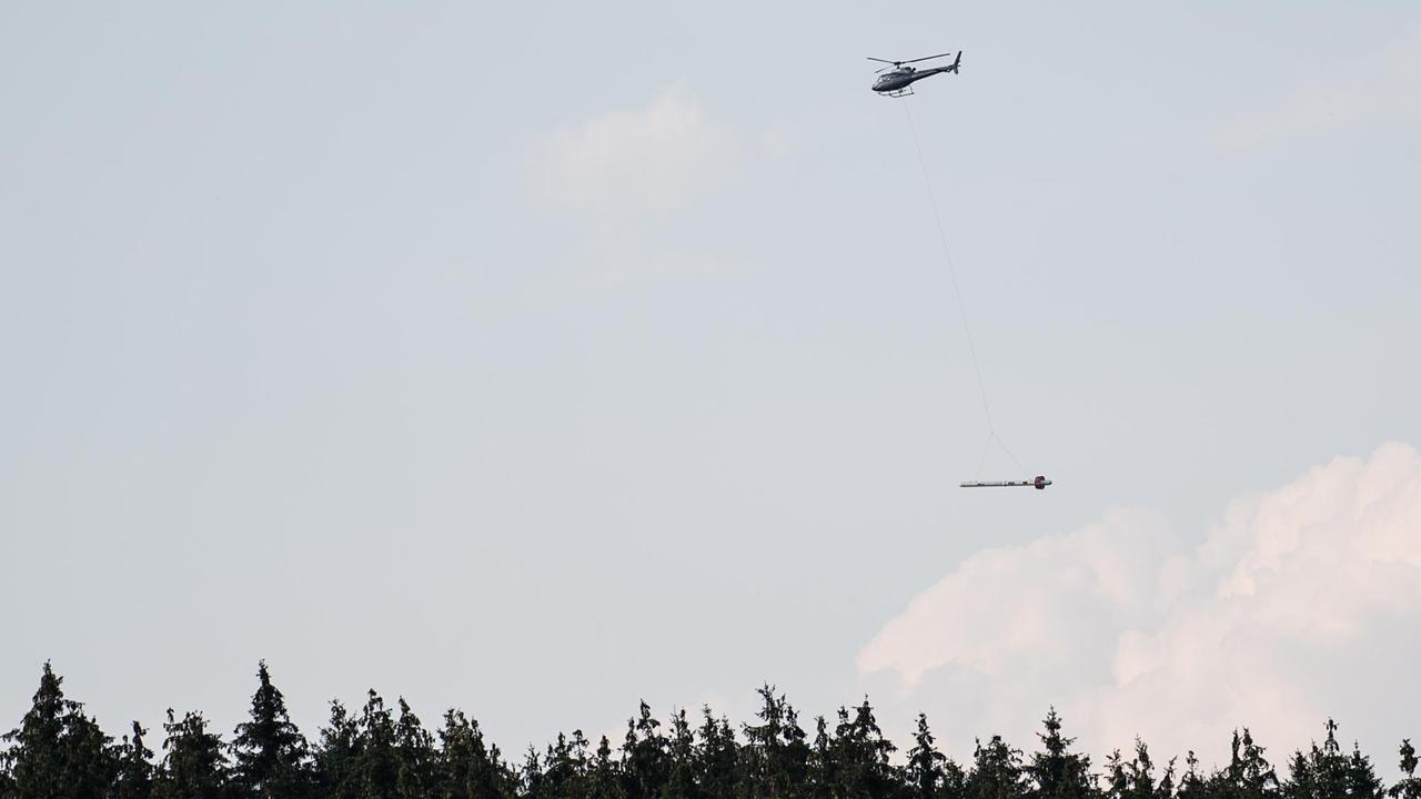 Ein Hubschrauber mit Messsonde fliegt über ein Waldstück. 