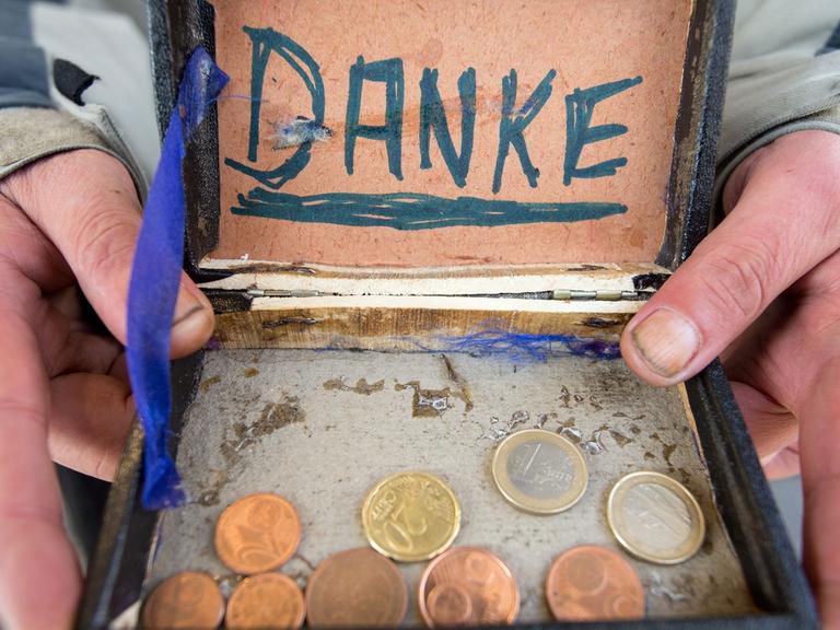 Ein Bettler hält eine alte Zigarrenkiste für Geldspenden in der Hand.