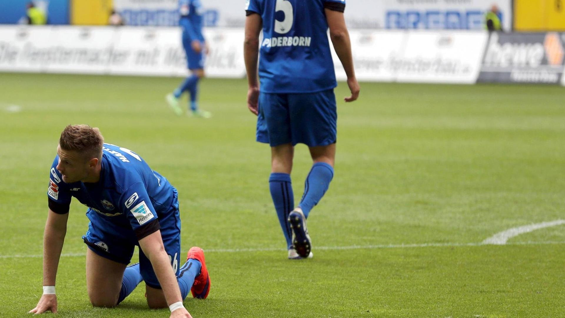 Ein Spieler des FC Paderborn kniet beim Spiel gegen den 1. FC Nürnberg am 15.05.2016 am Boden - im Hintergrund lässt ein Mitspieler den Kopf hängen. Der Verein steigt in die dritte Liga ab.