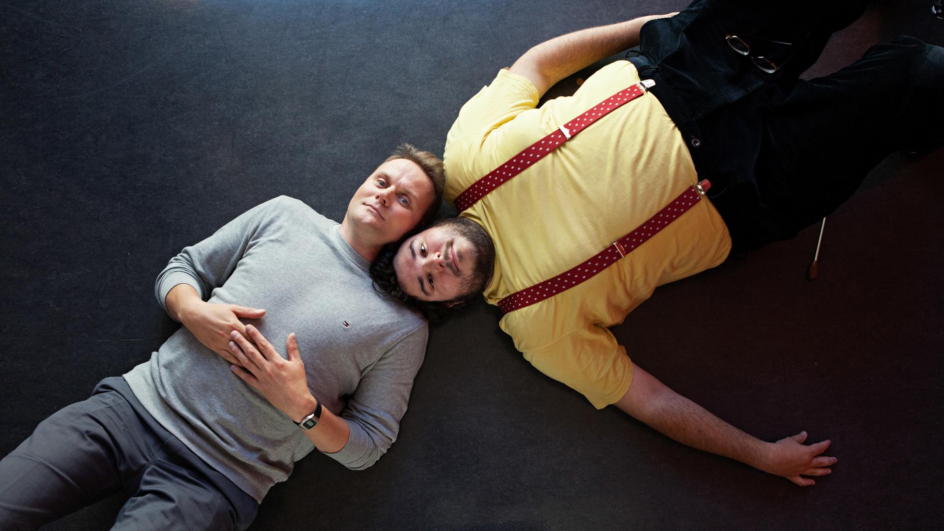 Devid Striesow und Axel Ranisch liegen auf dem Boden, die Köpfe nebeneinander