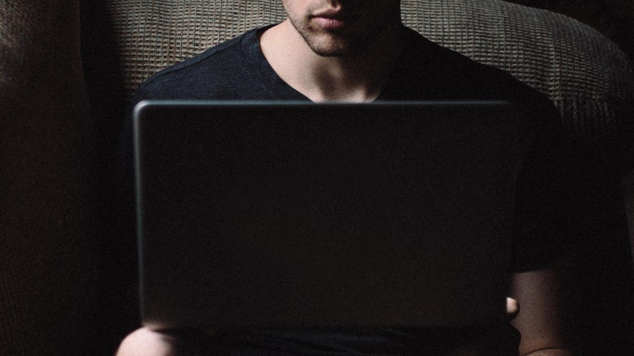 Ein Mann sitzt mit einem düsteren Gesichtsausdruck vor seinem Laptop.