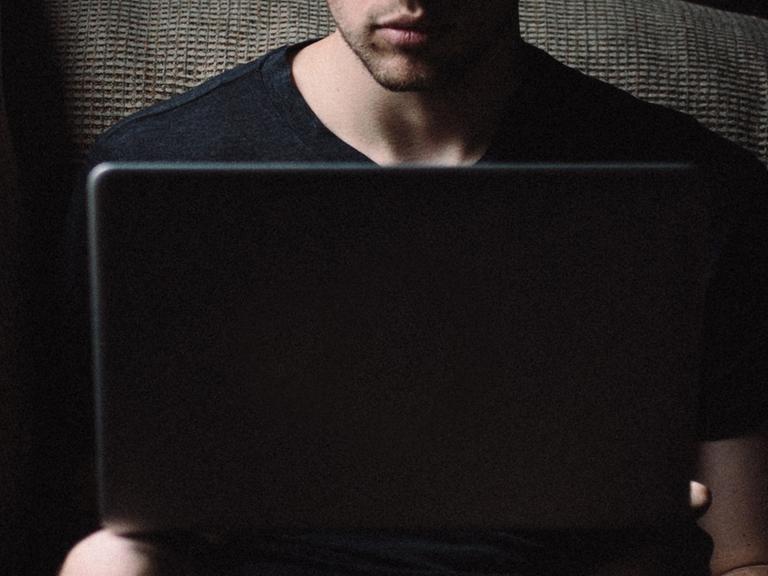 Ein Mann sitzt mit einem düsteren Gesichtsausdruck vor seinem Laptop.