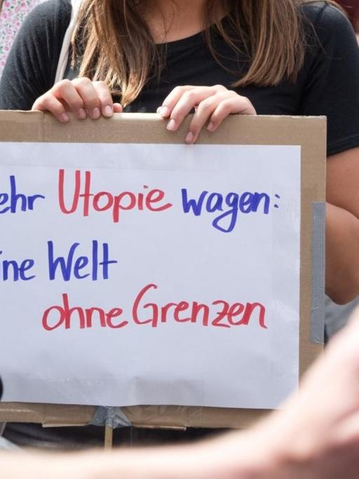 Eine Demonstrantin in Berlin-Kreuzberg hält bei Protesten für ein Bleiberecht für Flüchtlinge ein Schild mit der Aufschrift "Mehr Utopie wagen: Eine Welt ohne Grenzen". (5.7.2014)