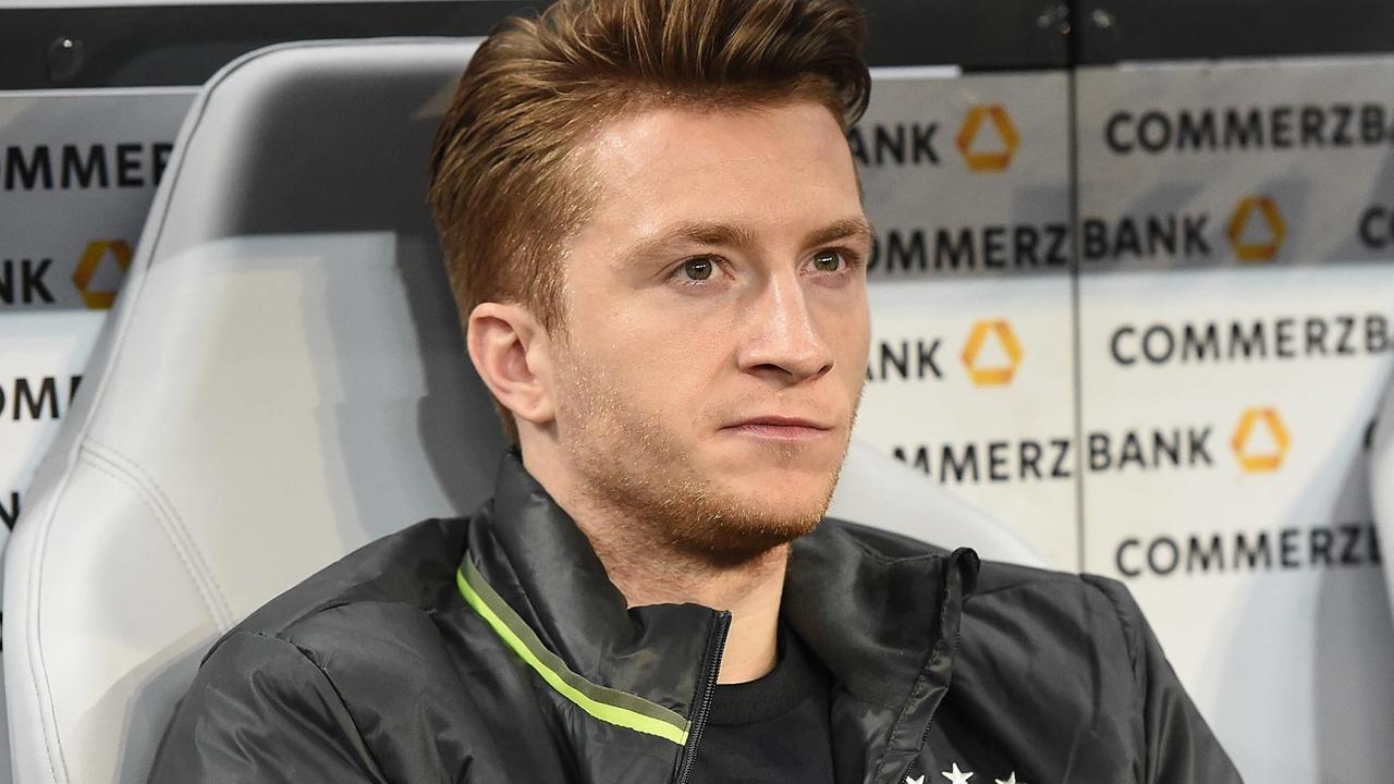 Reus sitzt mit ernstem Blick im schwarzen DFB-Trainingsanzug auf der Ersatzbank.