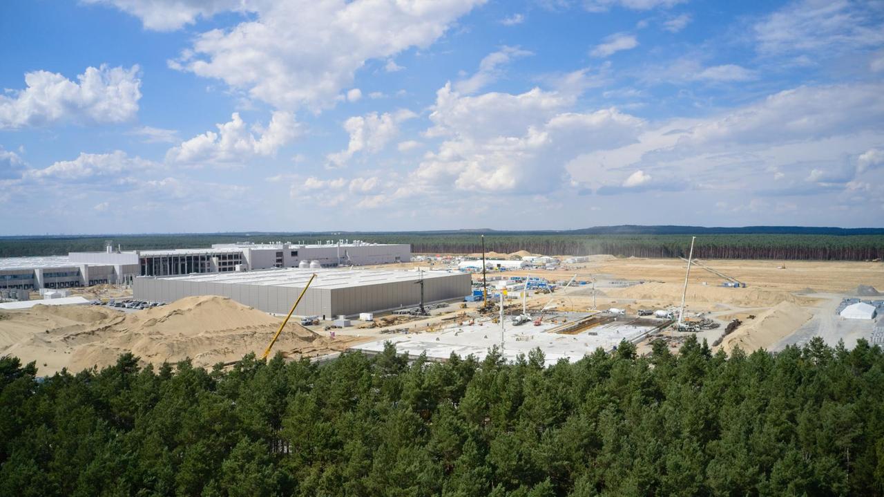  Blick auf die Tesla-Baustelle in Grünheide in Berlin, im Vordergrund Wald, im Hintergrund der Betonbau der Gigafactory.