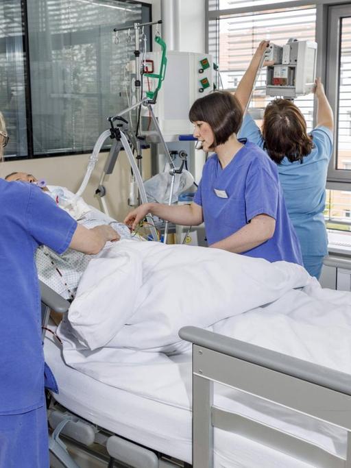 Drei Krankenschwestern stehen bei einem Patienten an einem Bett im Krankenzimmer mit Geräten der Intensivmedizin.