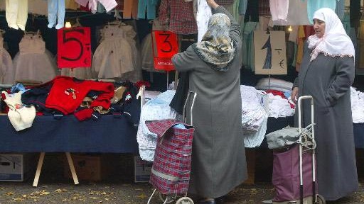 Zwei Frauen bekleidet mit langen Mänteln und Kopftuch schauen sich die Kleidung an einem Marktstand an.