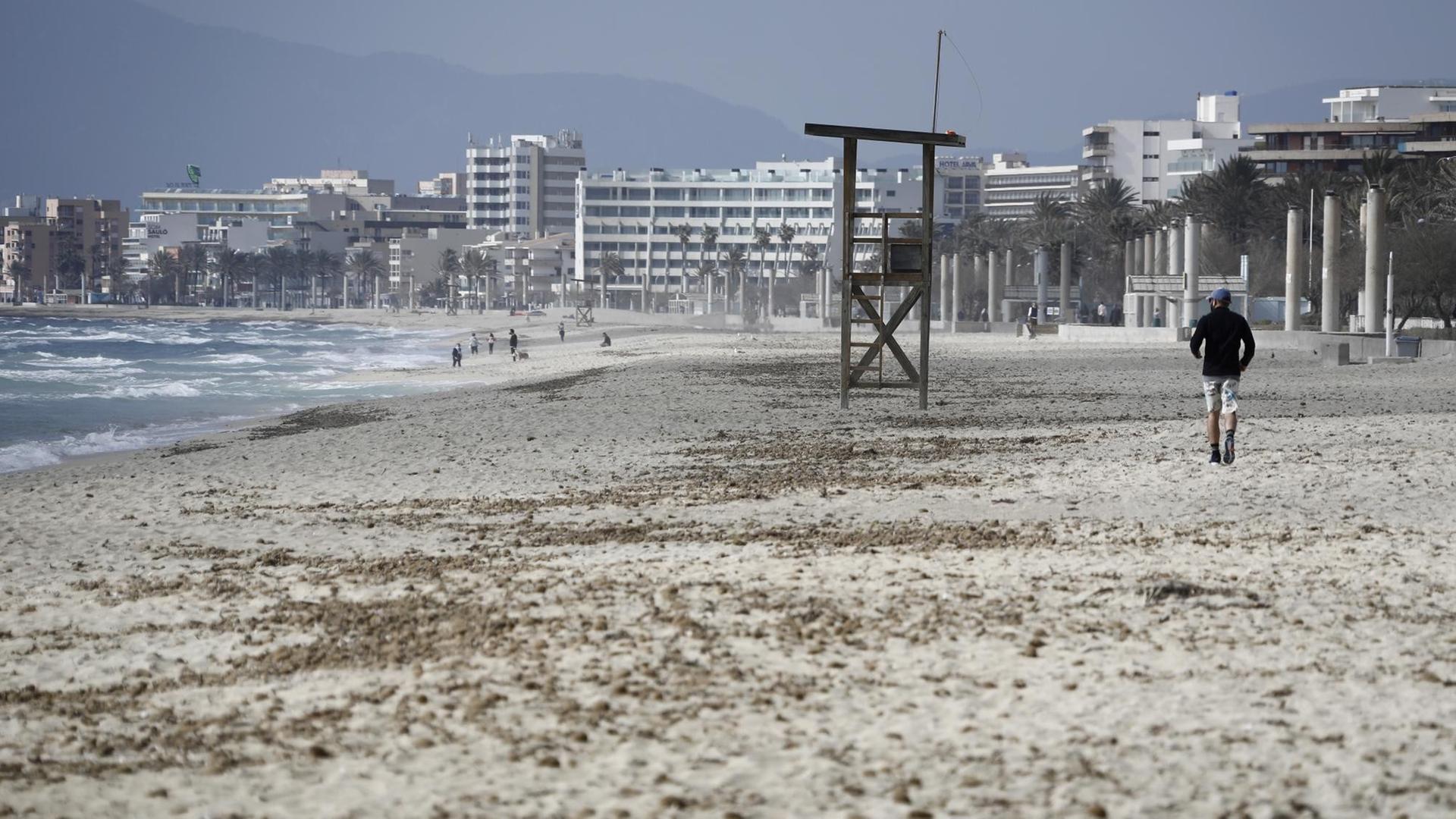 Ein Mann geht am Strand von Arenal auf Mallorca über den Sand. Deutsche Reiseveranstalter hoffen, dass sie Urlauber ab den Osterferien wieder nach Mallorca bringen können.