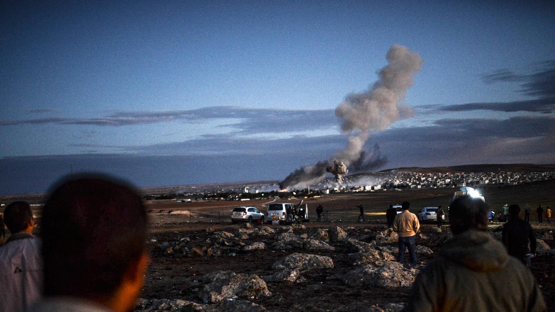 Menschen schauen aus der Ferne auf Kobane - über der Stadt sind Rauchwolken zu sehen.