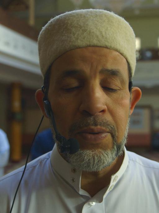 Der Imam Mohamed Taha Sabri steht in einer Szene aus dem Film "Inschallah" mit geschlossenen Augen in der Neuköllner Moschee, die er leitet.