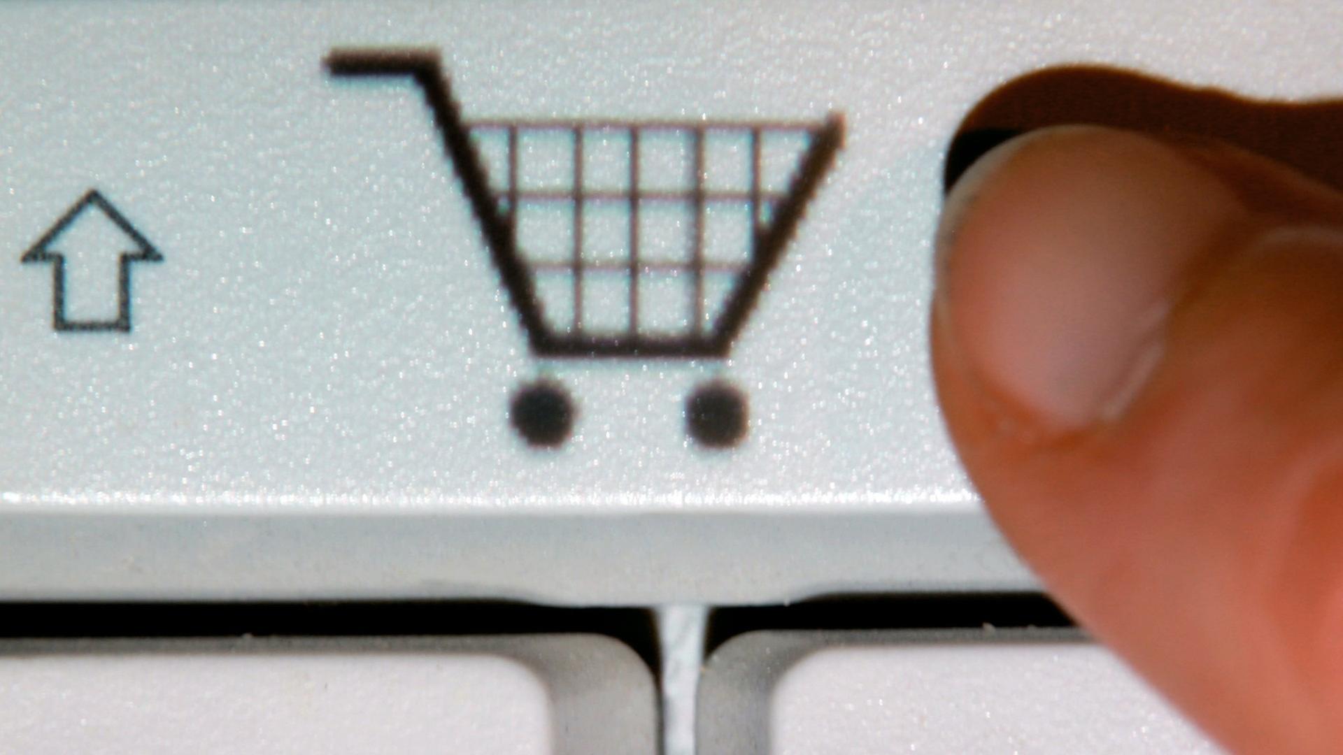 Ein Finger zeigt auf das Symbol eines Einkaufwagens auf einer Taste einer Computertastatur (gestelltes Foto).