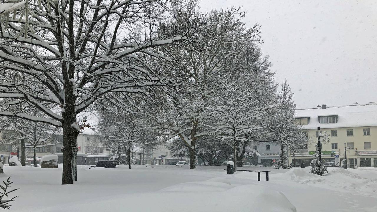 Blick auf das verschneite Stadtzentrum von Neugablonz, im Vordergrund Bäume, dahinter eine Straße mit schmuckloser 50er-Jahre-Architektur.