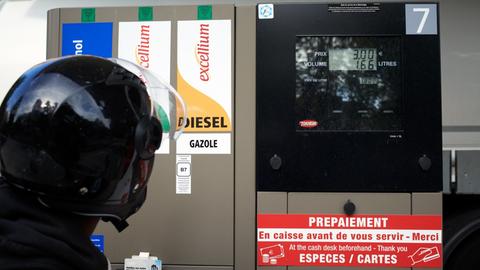 Mann mit Motorradhelm blickt auf Zapfsäule