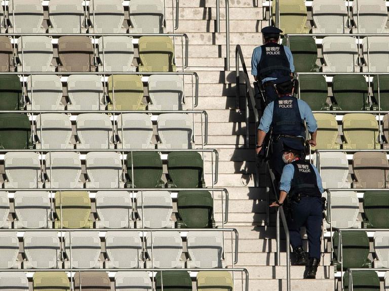 Eröffnungsfeier im Olympiastadion von Tokio. Polizisten gehen die leere Tribüne hoch.