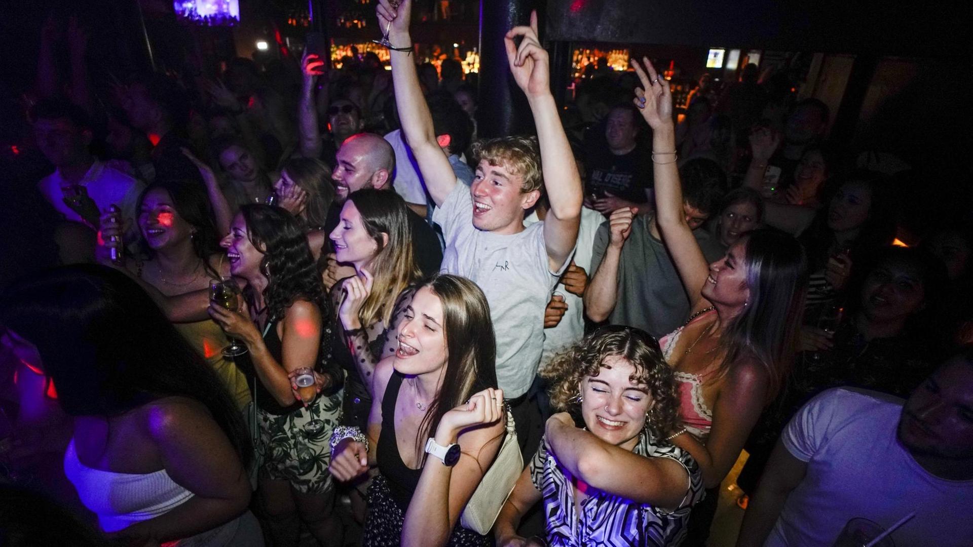 Junge Menschen feiern in einem Club. Sie tragen keine Masken und tanzen eng nebeneinander - so wie vor der Corona-Pandemie.