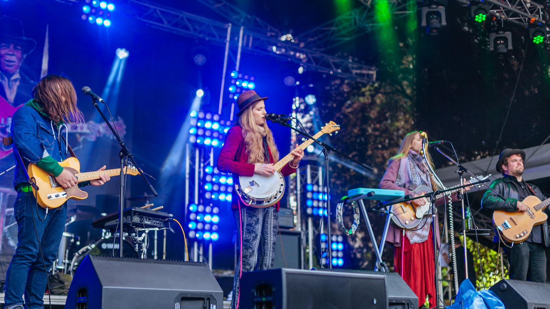 Eine Band, bestehend aus zwei Frauen und zwei Männern, steht auf einer Festivalbühne und spielt.