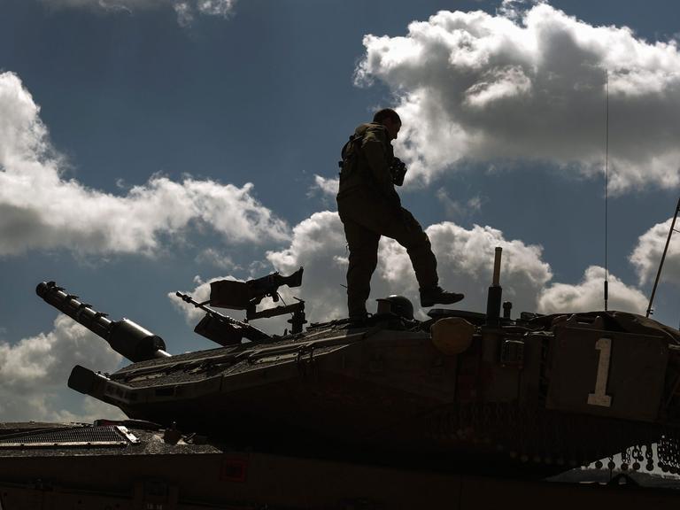 Ein Soldat steht auf einem Panzer, am Himmel viele Wolken.