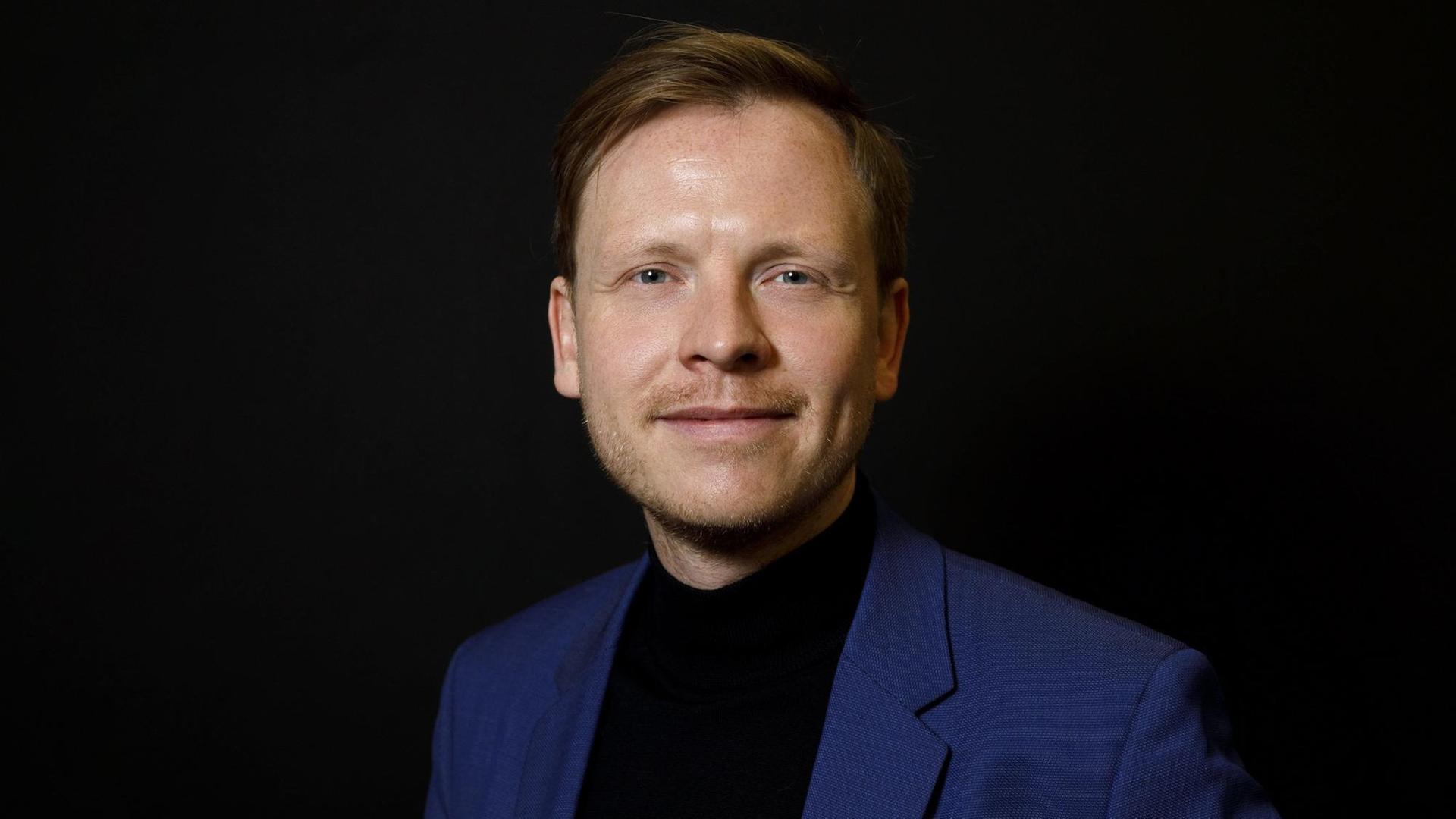 Markus Gabriel steht vor schwarzem Hintergrund und blickt freundlich in die Kamera.