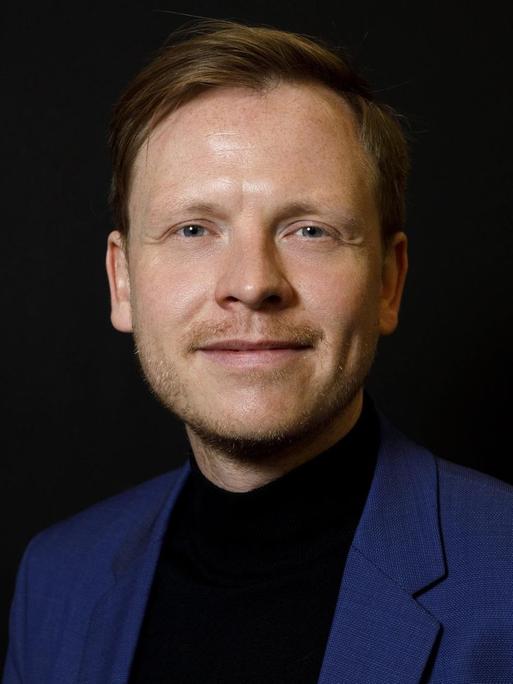 Markus Gabriel steht vor schwarzem Hintergrund und blickt freundlich in die Kamera.
