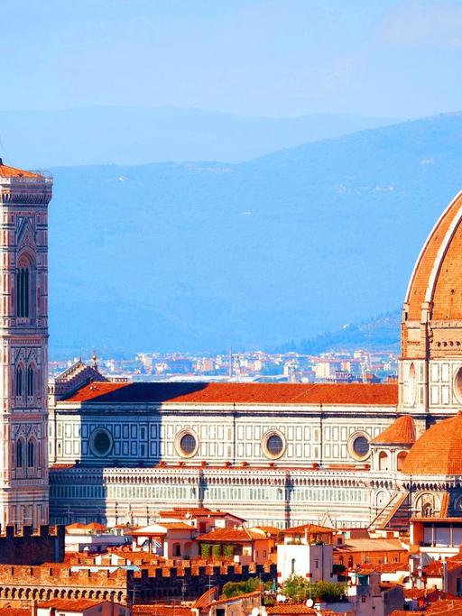 Ein Farbfoto zeigt das Panorama von Florenz mit mit rotziegelten Dächern. Die Hügel der Toskana im Hintergrund Davor die Kuppel des Doms und der Campanile