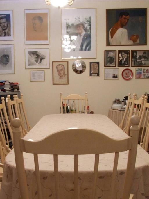 Eine Tafel mit leeren Stühlen in einem Wohnzimmer. An der Wand hängen Bilder.