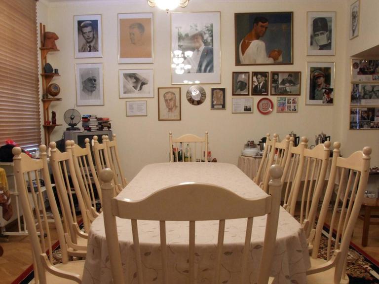Eine Tafel mit leeren Stühlen in einem Wohnzimmer. An der Wand hängen Bilder.