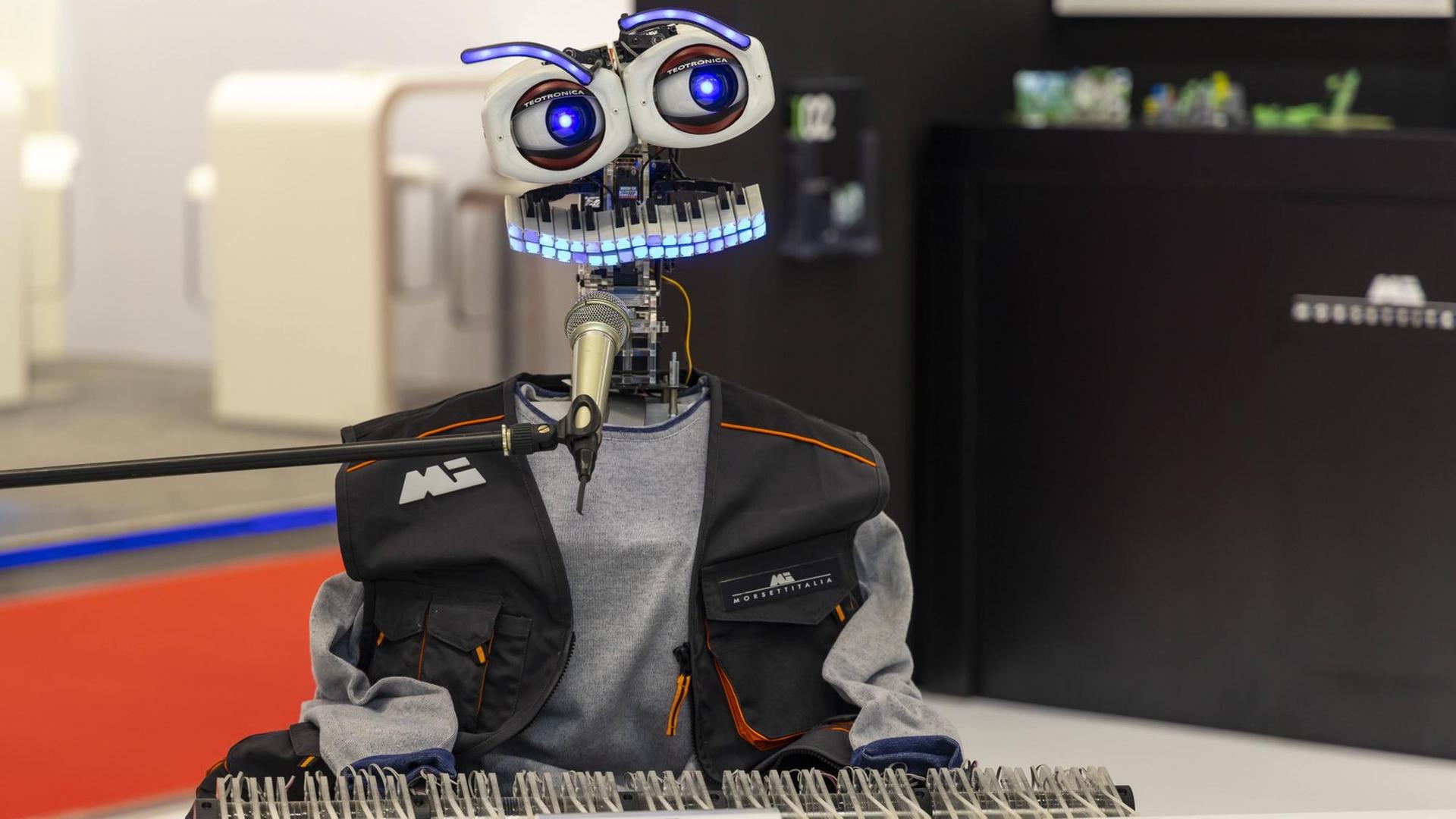 Ein Roboter mit Tastaturmund und großen Augen sitzt vor einer Klaviatur und Mikrofon und scheint zu musizieren.