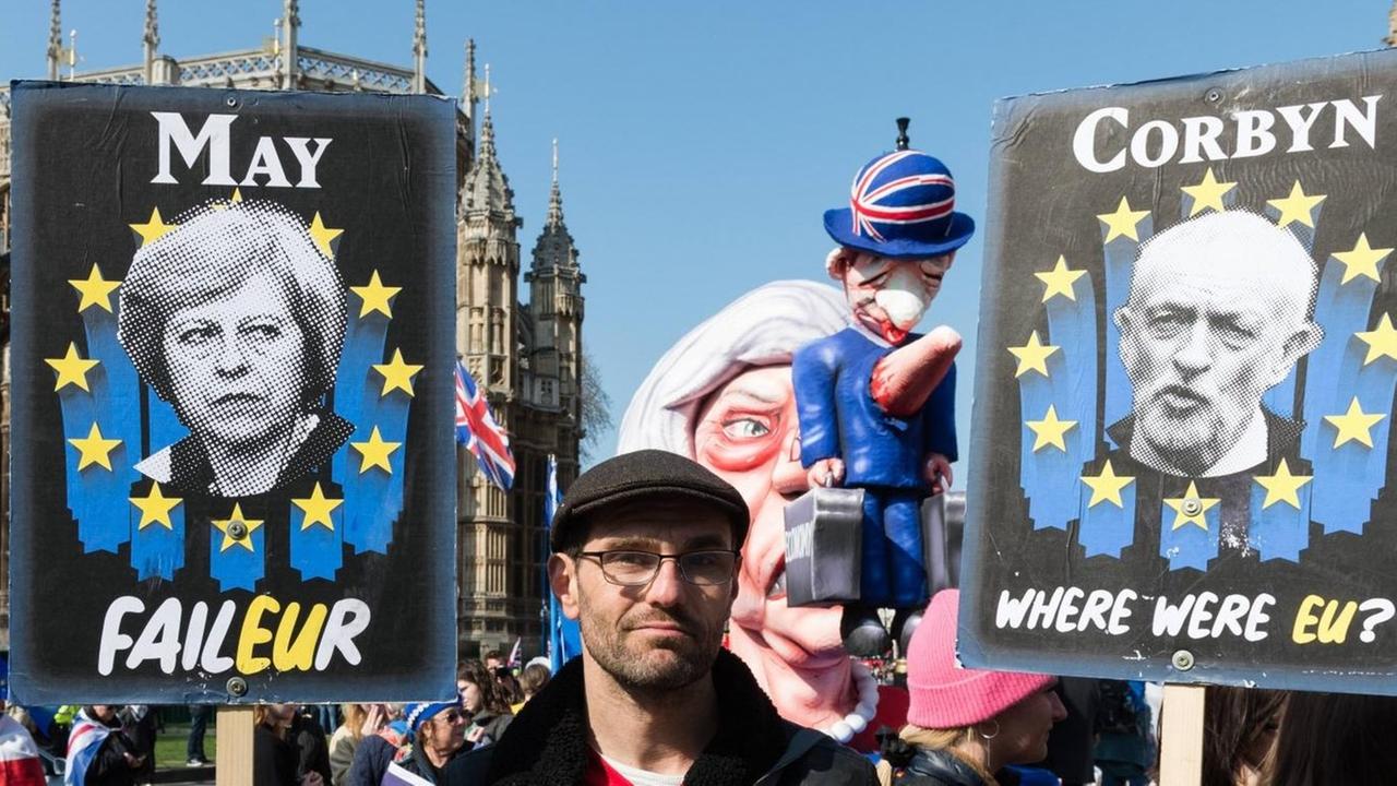Ein Anti-Brexit-Demonstrant hält Plakate von May und Corbyn in den Händen