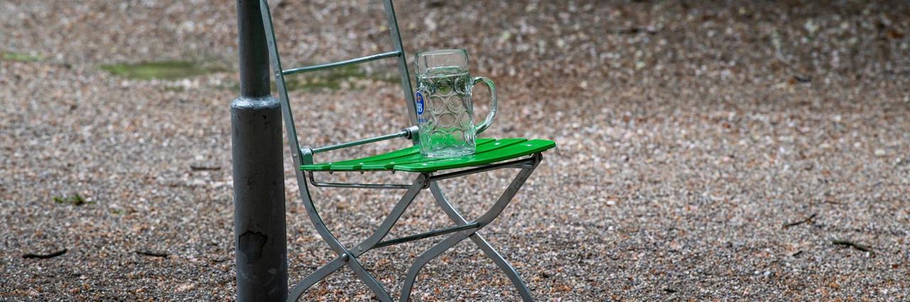 Ein leerer Maßkrug auf einem einzelnen Klappstuhl steht im Biergarten am Chinaturm in München, Mai 2020. Ein leerer Maßkrug auf einem einzelnen Klappstuhl steht im Biergarten am Chinaturm in München, Mai 2020.