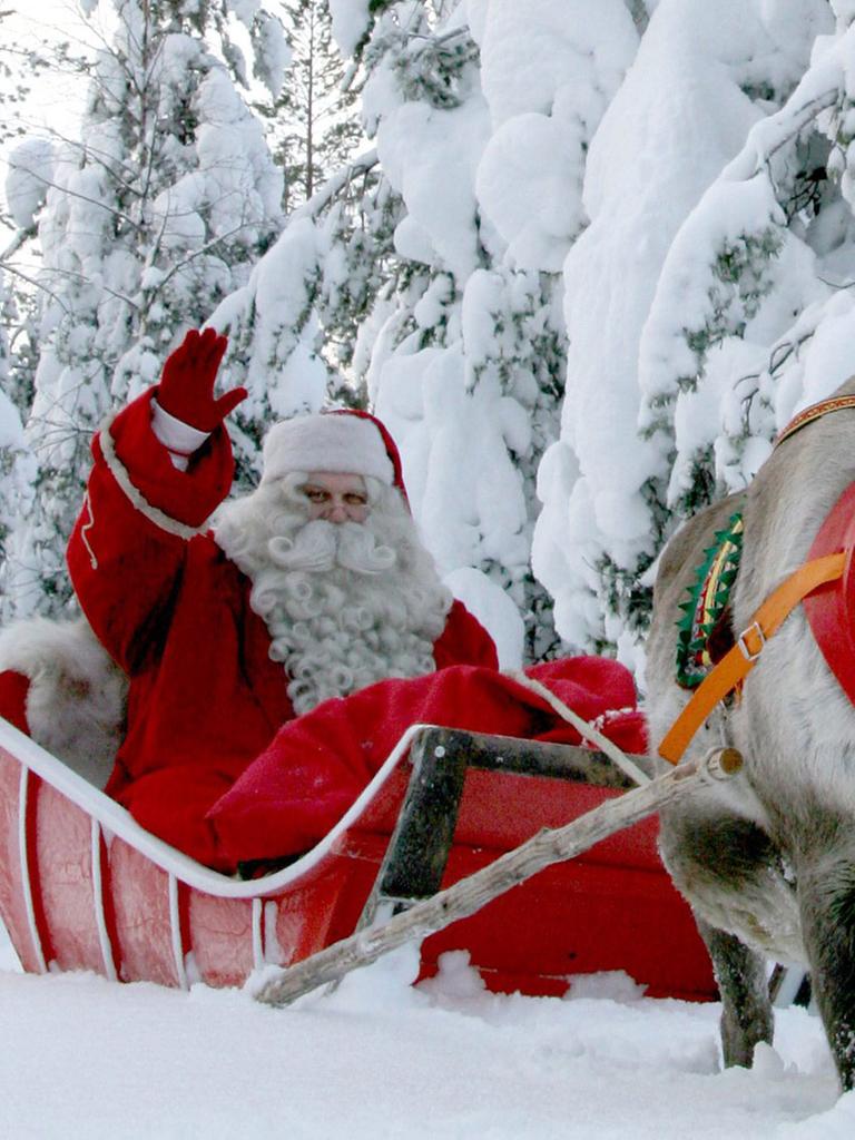 Ein als Weihnachtsmann oder Nikolaus verkleideter Mann sitzt auf einem Schlitten, der von einem Rentier gezogen wird. Im Hintergrund sieht man schneebedeckte Tannen.