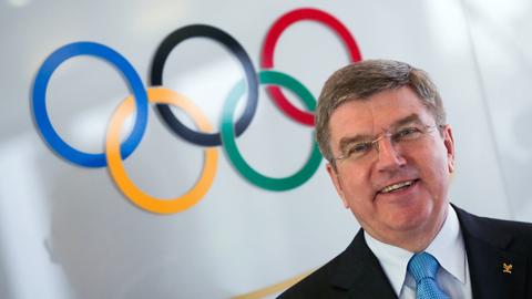 Der Präsident des Internationalen Olympischen Komitees, Thomas Bach, lächelnd vor den Olympischen Ringen.