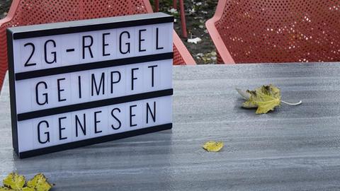 Auf einem Tisch steht ein Leuchtkasten mit den Schriftzuegen "2G-Regel, geimpft und genesen".