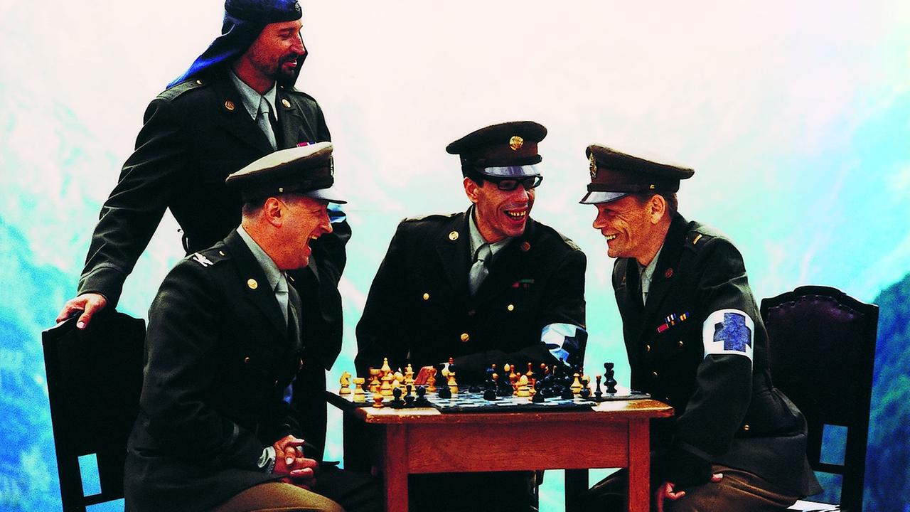 Die Musiker der Band Laibach sitzen in Uniformen um einen Tisch mit Schachspiel zusammen.