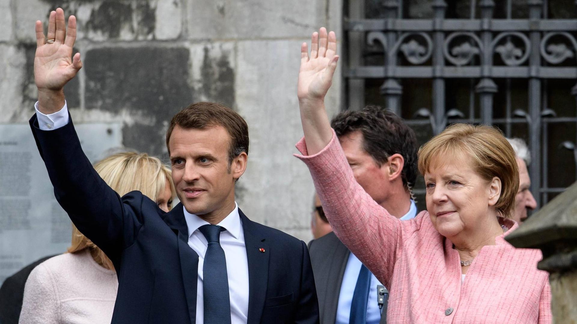 Bundeskanzlerin Angela Merkel (CDU), und der französische Staatspräsident Emmanuel Macron winken in die selbe Richtung.