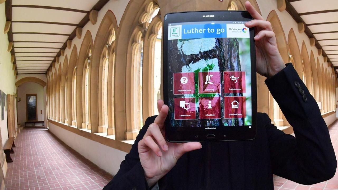 Im Kreuzgang des Augustinerklosters präsentiert eine Frau am 12.07.2016 in Erfurt (Thüringen) ein Tablet, auf dessen Bildschirm die neue Luther-App zu sehen ist. Sie wurde am selben Tag von der Thüringer Tourismus GmbH (TTG) vorgestellt.