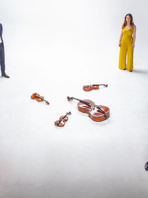 In der Mitte eines weißen Raumes liegen vier Streichinstrumente, und jeweils ein Stück entfernt stehen die entsprechenden Interpreten. Die beiden Frauen tragen auffälliges Rot und Gelb, die Männer blaue Anzüge.