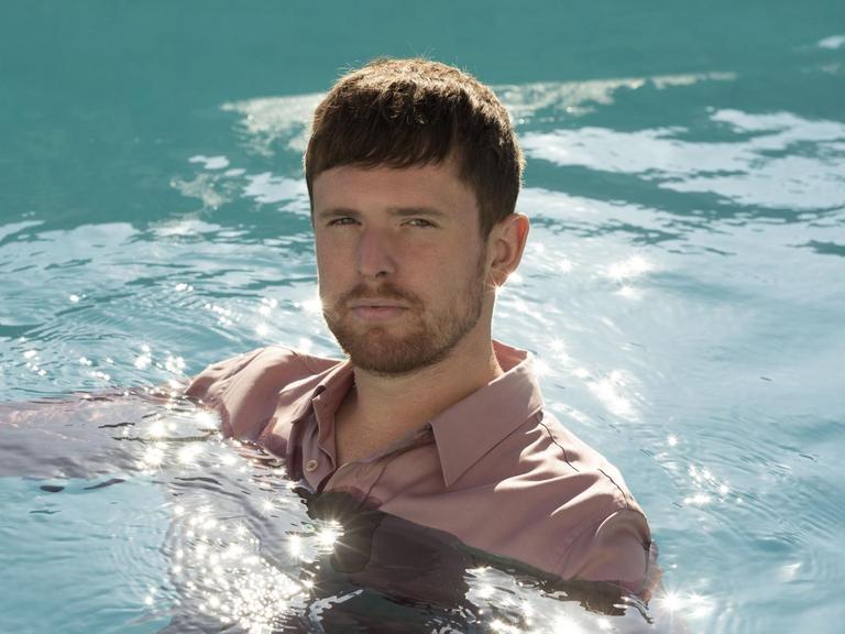 James Blake schwimmt in einem Pool und trägt dabei ein rosa Hemd